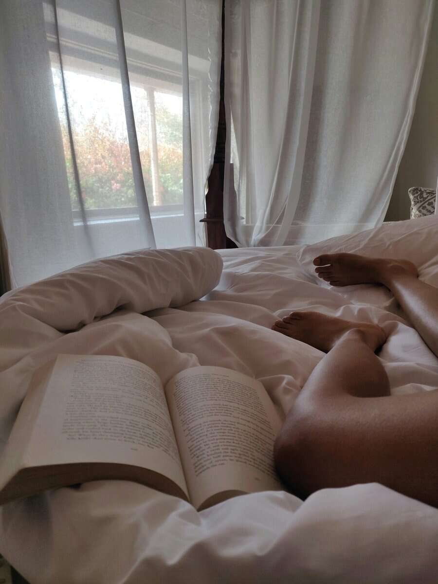 A peson's bare legs with a presumably spicy book open besides them.